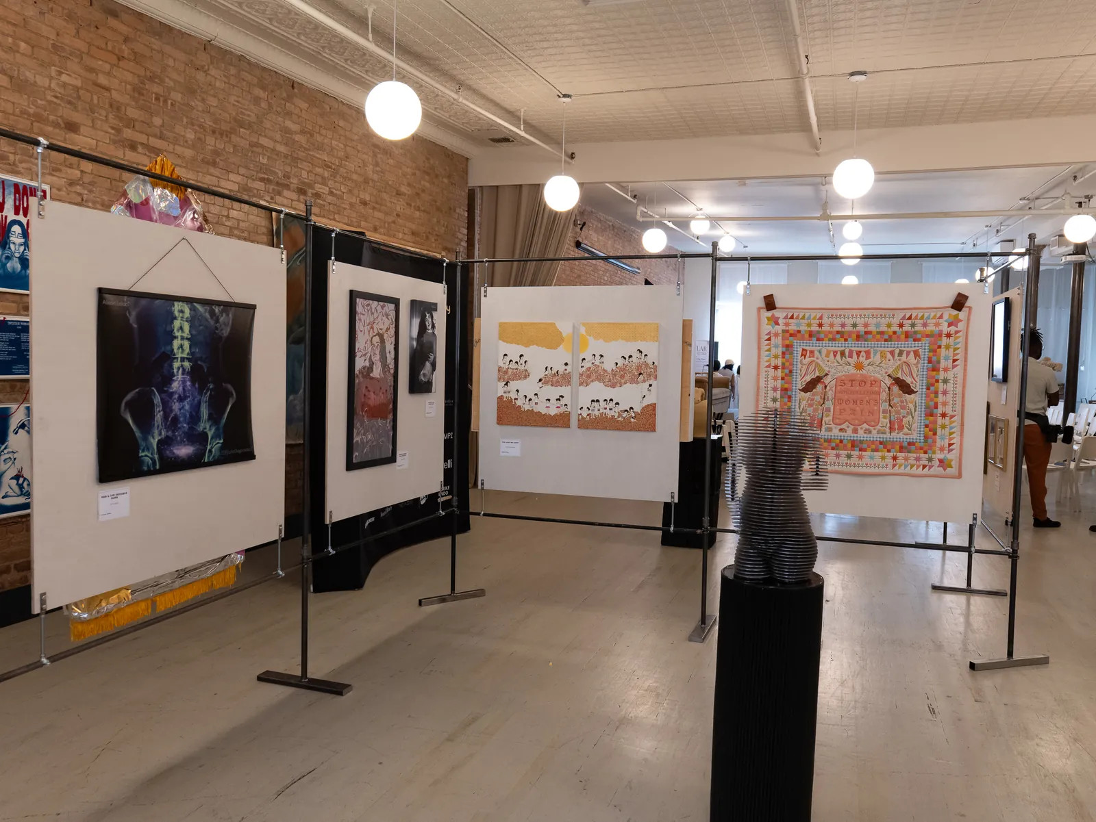 The TRELLIS steel framework set out across the Annex, plywood panels hung from its rails holding an X-ray print, paintings and a bright quilt, with the stacked-steel sculpture Waiting for You on a black plinth in the foreground.