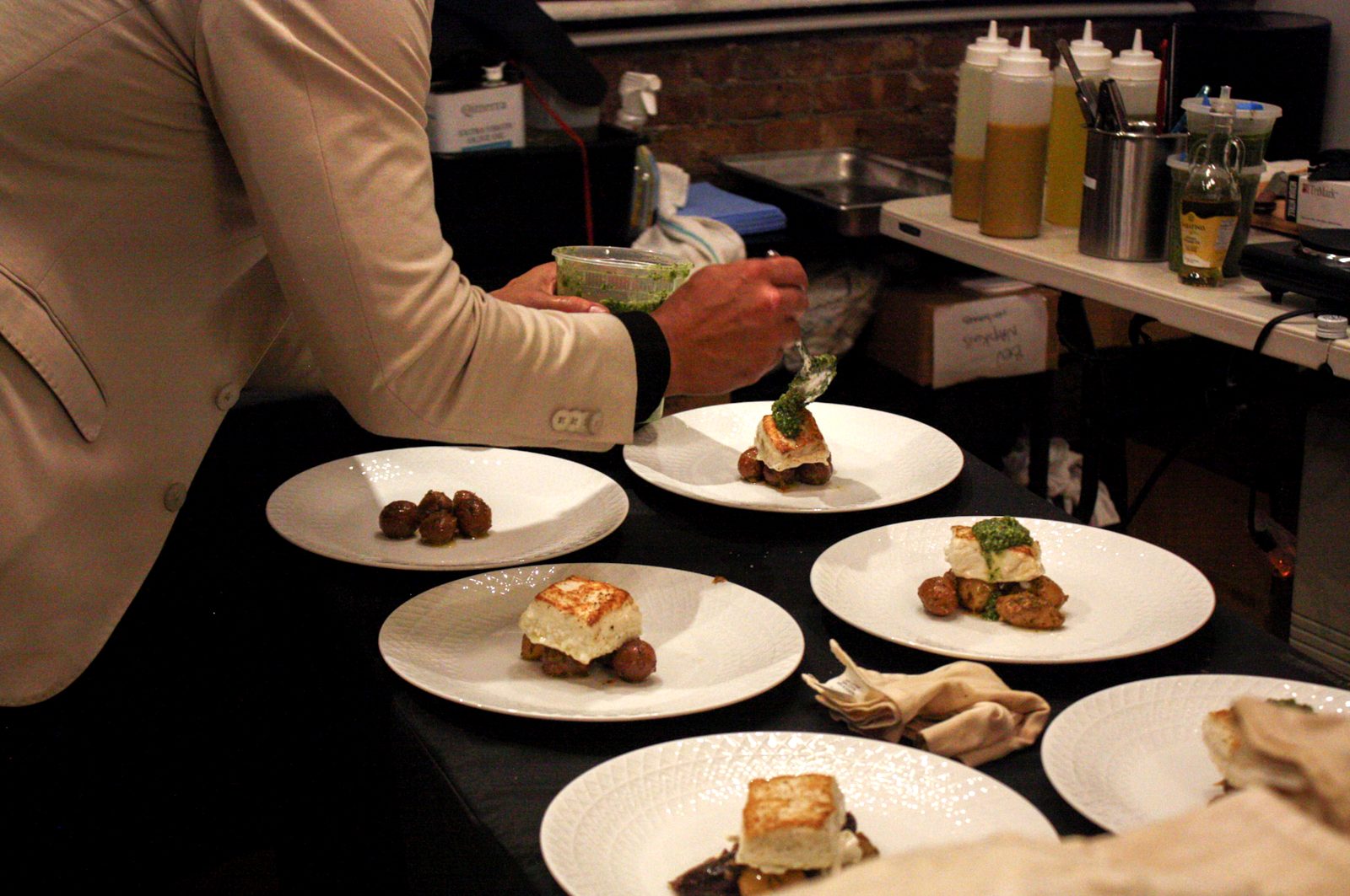 Pesto spooned onto the halibut as plates are finished on a black table