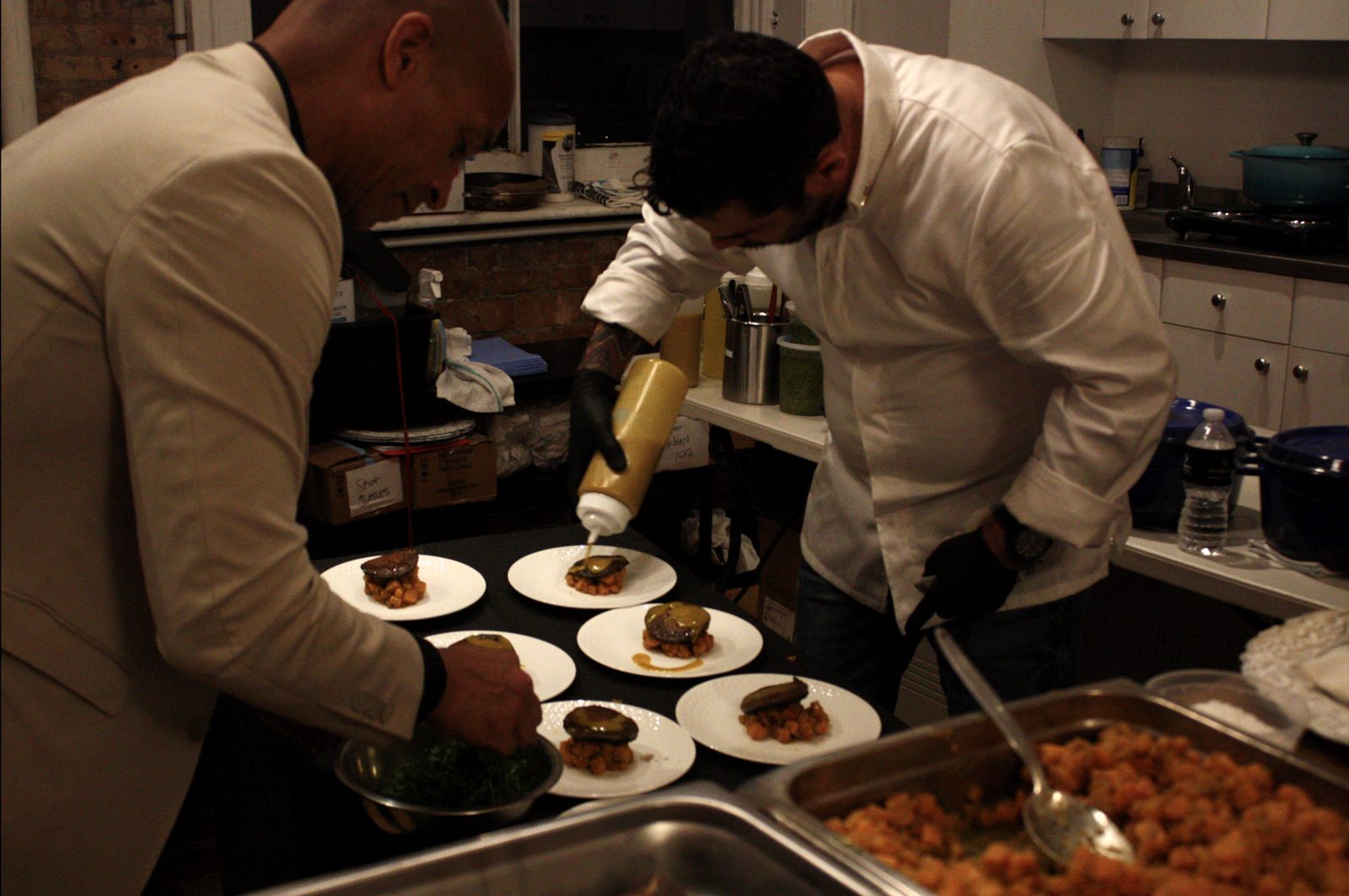 Two cooks plate the portobello course, one piping sauce from a squeeze bottle