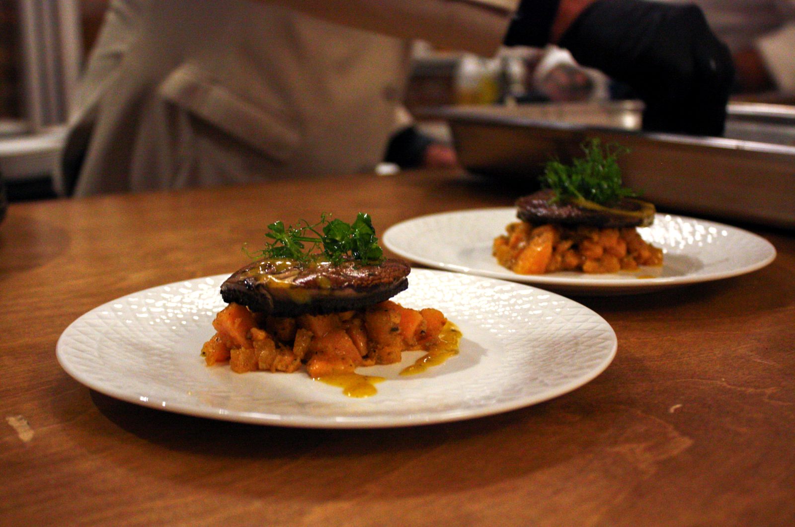 Two plates of roasted portobello over diced sweet potato, topped with pea shoots