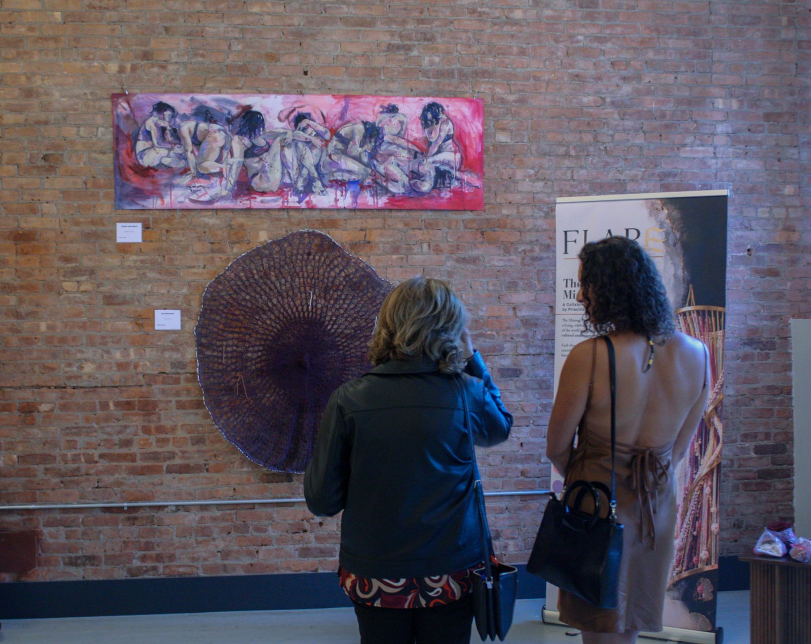 Two visitors stand before the knitted work, beside the banner for The Missing Piece