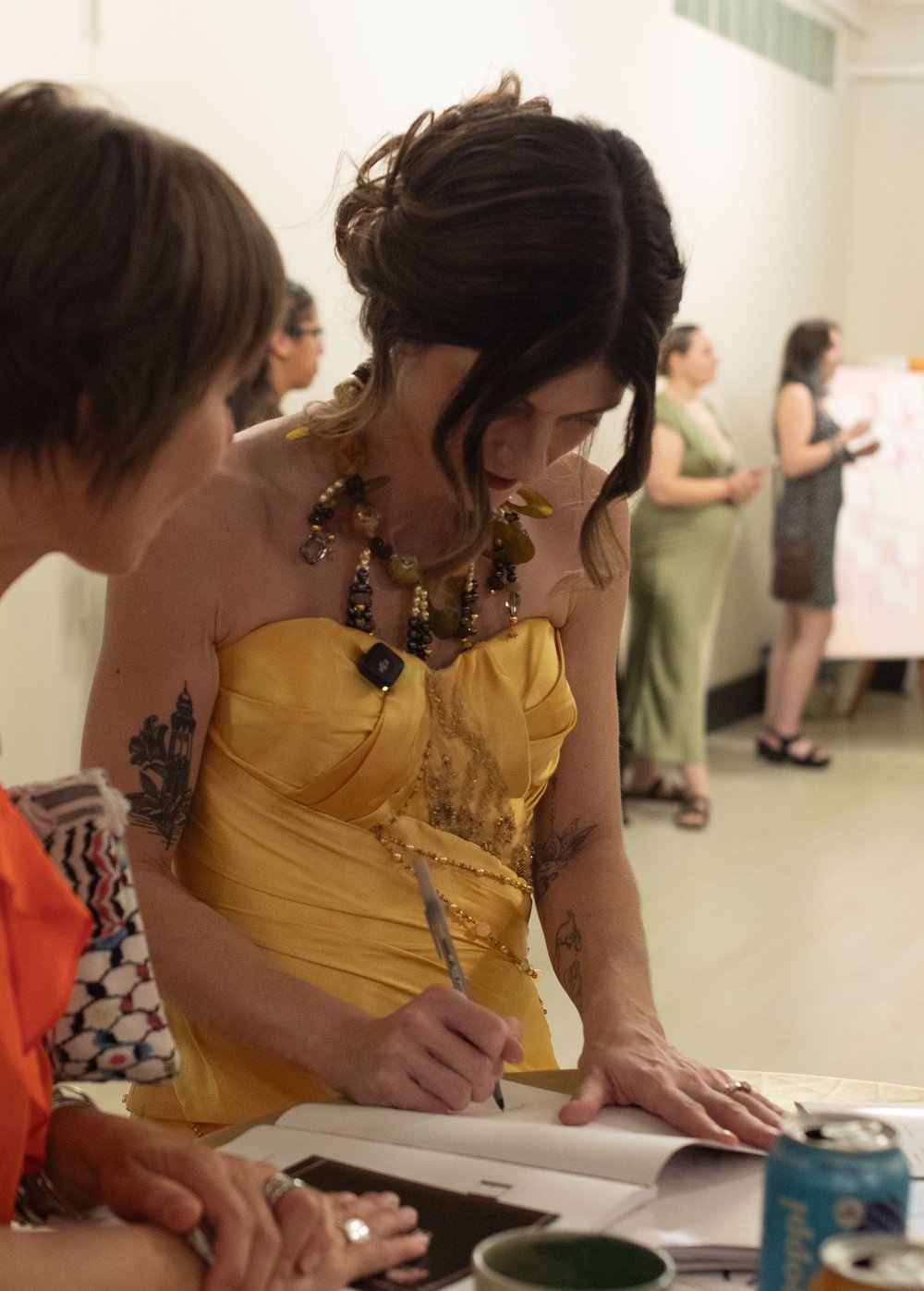 Priscilla Smith, in the gold dress and beaded necklace, signs a copy of her book for a guest at a high table.