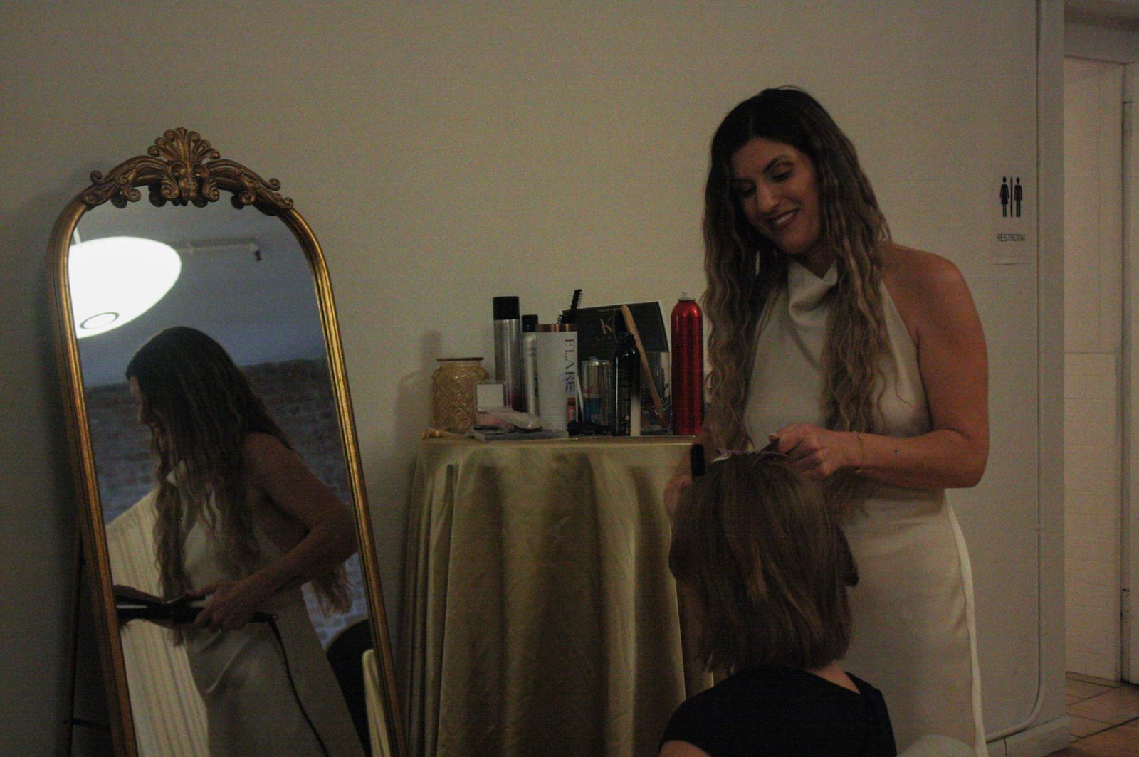 Caroline Palmieri styles a guest&rsquo;s hair in the Self-Care Lounge, beside a gold-framed mirror