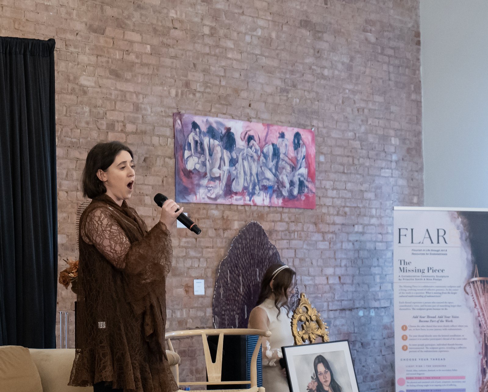 Ann-Marie Iacoviello singing into a handheld microphone beside the banner for The Missing Piece
